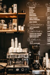 A coffee wall with the entire menu written on it on black board. Coffee machine, with cups placed on the side. Visible coffee beans, elevating the look of the ambience.