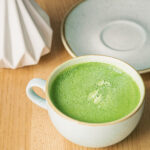 Close-up, a large ceramic cup with a green matcha drink on a wooden table in a cafe.