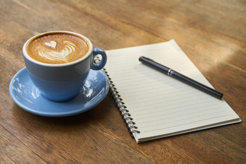 coffee with foam art on a wooden table with a notebook and a pen