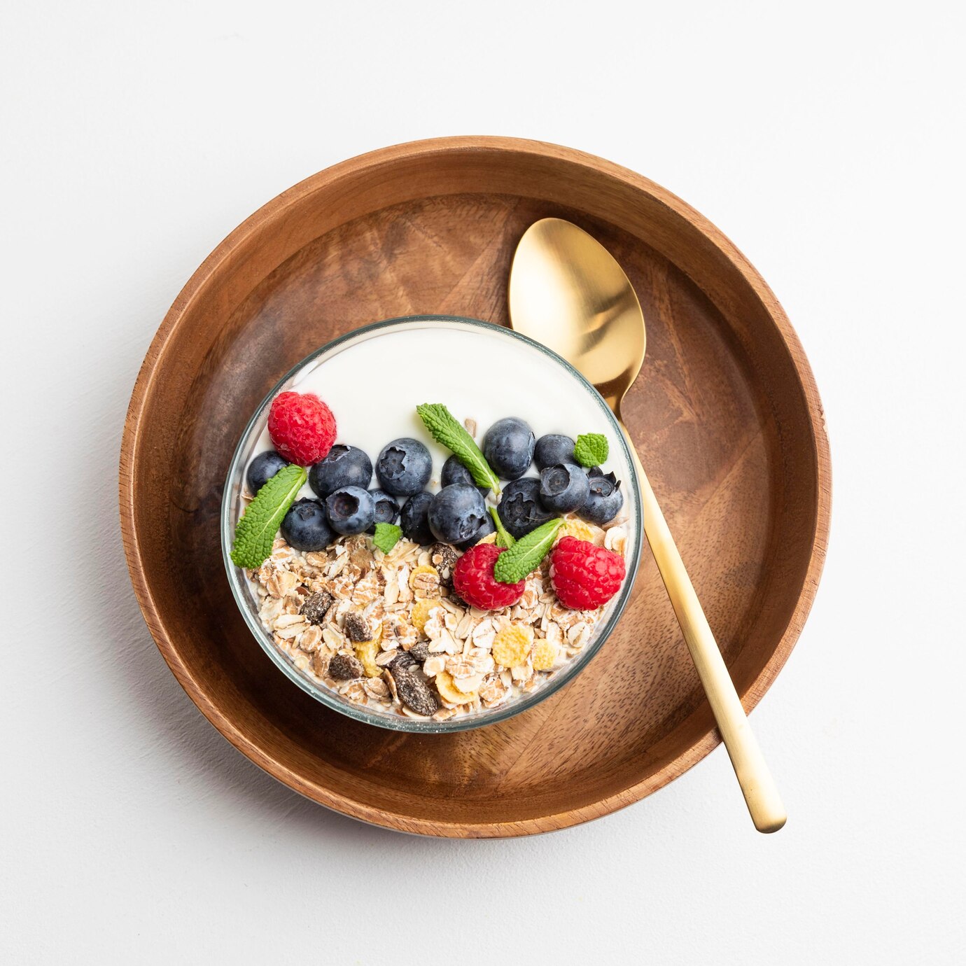 top view of a breakfast bowl with raspberries and blueberries placed on a wooden plate and golden spoon in a cafe with healthy snacks