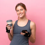 Young woman holding a reusable coffee cup and smiling after a gym session.