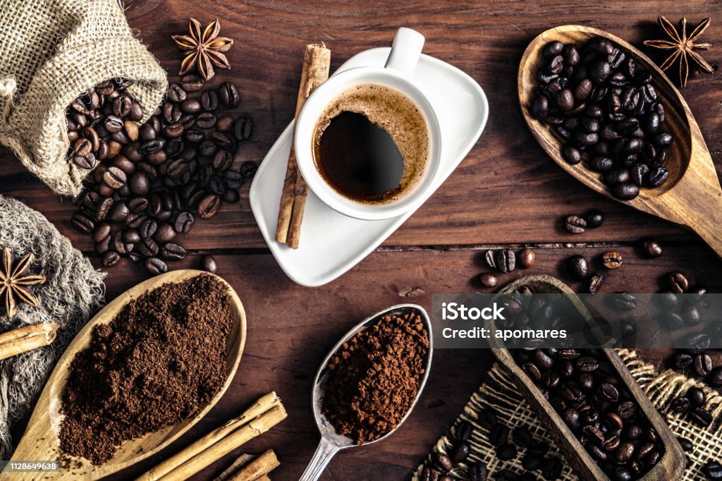 Herbal coffee quiet workspace Mississauga: Dark roast coffee beans, ground coffee, and brewed coffee in a white cup on a wooden table with cinnamon sticks and star anise.