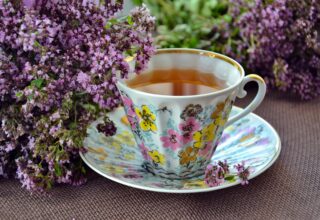 A floral teacup filled with herbal tea, surrounded by fresh purple blossoms, creating a peaceful and aromatic tea experience.