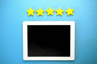 A white tablet with a black screen placed on a blue background with five yellow stars above it, symbolizing a five-star rating or digital excellence.