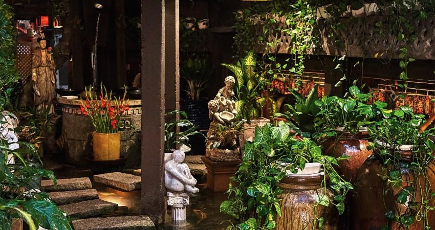 A cafe with a lot of potted plants and statues.